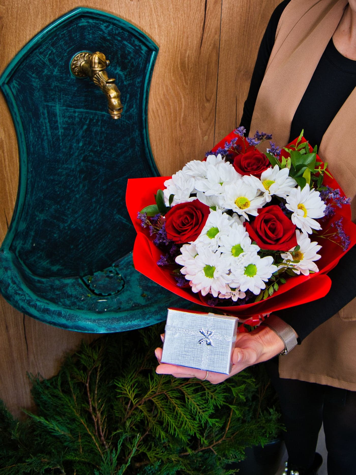 Floristka z Květiny spolu drží kytici z červených růží a bílých chryzantém s malým dárkem