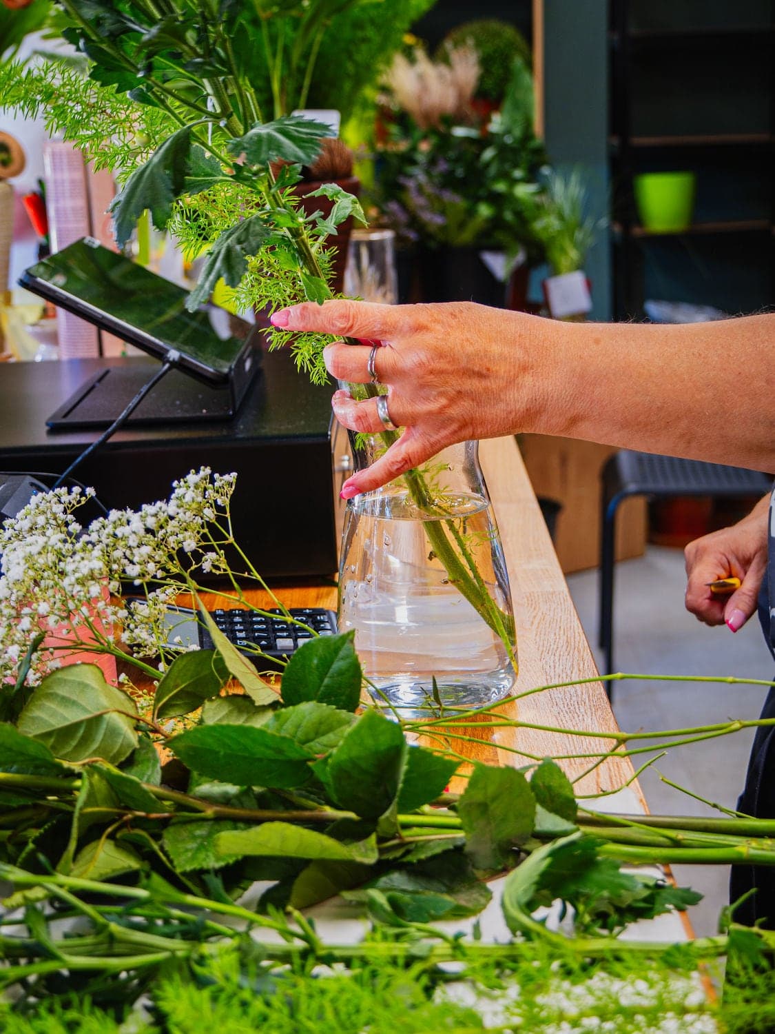 Floristka aranžuje květiny do vázy na pultu květinářství Květiny spolu
